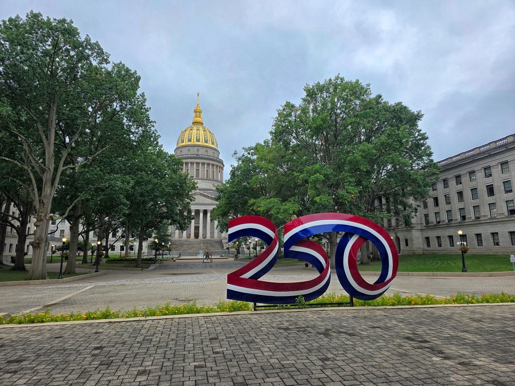 Eine Skulptur mit der Zahl 250 in Rot, Weiß und Blau steht vor einem Gebäude mit goldener Kuppel. Grüne Bäume säumen den Platz im Hintergrund